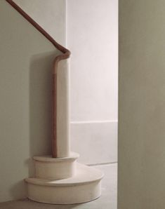 a white staircase with a wooden handrail on the top and bottom, next to a wall