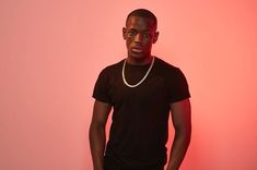 a man standing in front of a pink wall wearing a black shirt and pearls necklace