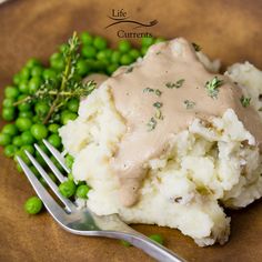 a plate with mashed potatoes, peas and gravy on it next to a fork