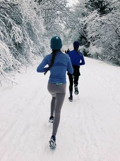 two people are running in the snow on cross country skis and one is wearing a blue jacket