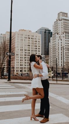 a man and woman kissing in the middle of a cross walk with tall buildings in the background