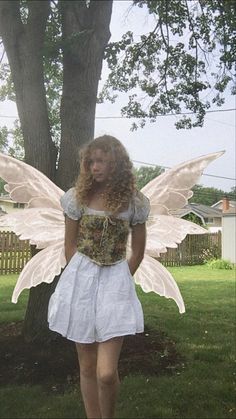 a woman dressed as a fairy standing next to a tree