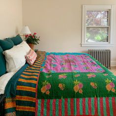 a bed with colorful blankets and pillows on top of it next to a window in a bedroom