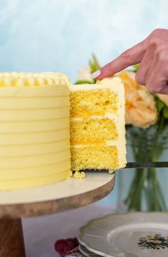 a person is cutting into a yellow cake on a table with flowers in the background