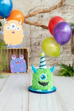 a birthday cake with monsters and balloons in the background on a wooden table, surrounded by other decorations