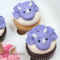 three cupcakes decorated with purple frosting and white icing, one has a unicorn horn on top