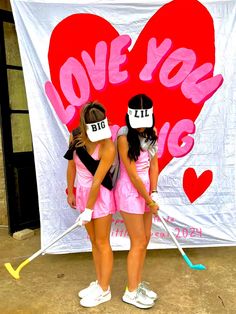 two girls in pink dresses are standing next to a giant love you big banner with the words