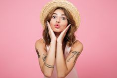 a woman wearing a straw hat and holding her hands to her face while making a funny face