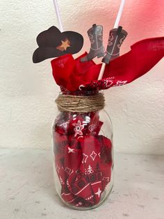 a glass jar filled with red candy and cowboy hats on top of a white table