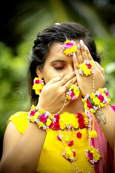 a woman covering her face with flowers and beads on her hands while looking at the camera