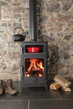 a wood burning stove sitting on top of a floor next to some logs and shoes