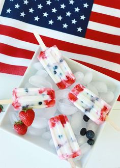 patriotic popsicles on a plate with strawberries and blueberries in front of an american flag