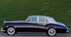 an old black car is parked on the side of the road in front of a grassy hill