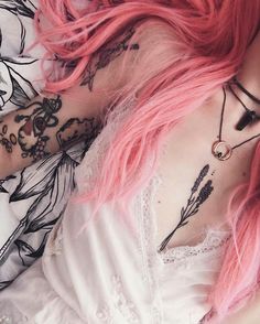 a woman with pink hair laying on top of a bed covered in tattoos and piercings