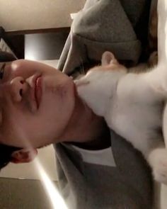 a man holding a white and gray cat up to his face while laying on top of a bed