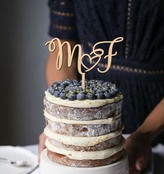 a person holding a cake with blueberries on top and the word m & f spelled in gold