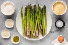 asparagus on a plate with eggs, flour and seasoning in small bowls