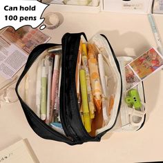 a black bag filled with pens and pencils on top of a white table next to an open notebook