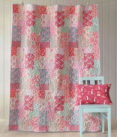 a chair sitting in front of a pink and green quilted wall hanging from a hook