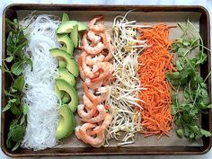 a tray filled with shrimp, carrots, avocado and rice noodles next to lettuce