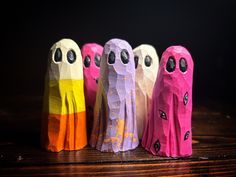 five different colored paper dolls are lined up in a row on a wooden table with black background