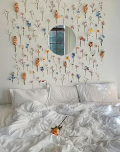 a bed with white sheets and flowers on the wall above it is shown in front of a round mirror