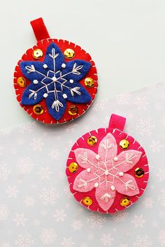 two red and blue ornaments sitting on top of a white table covered in snowflakes