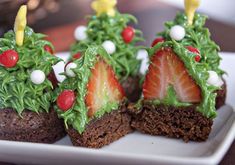 some brownies are decorated with green icing and strawberries on top, as well as christmas trees