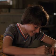 a young boy sitting at a table with a laptop computer in his hand and smiling