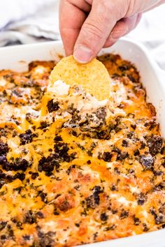 a hand dipping a tortilla chip into a casserole dish with cheese and black olives