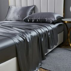 a bed with silver sheets and pillows on top of it next to a night stand