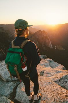 a person with a backpack standing on top of a mountain looking out at the sunset