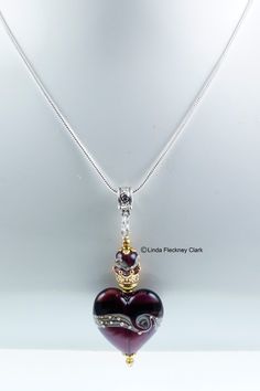 "I have created this one-of-a-kind 'Hera Heart' pendant necklace from a lampwork glass heart focal and matching spacer bead, gold plated brass crown bead, gold plated brass and pewter spacer beads and bead caps, silver plated brass jewellery wire and bale, silver plated brass snake chain and a lobster clasp Alt Text Necklace of a lampwork glass heart focal and matching spacer bead, gold plated brass crown bead, gold plated brass and pewter spacer beads and bead caps, silver plated brass jeweller Elegant Glass Jewelry With Heart Charm, Glass Heart Bead Pendant Jewelry, Pendant Necklace With Bead Caps For Gifts, Pendant Jewelry With Bead Caps For Gift, Pendant Necklaces With Bead Caps For Gifts, Glass Heart Pendant With Heart Beads, Heart Shaped Spacer Beads Jewelry For Gifts, Unique Necklaces With Bead Caps For Gifts, Elegant Keepsake Necklaces With Heart Beads