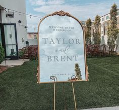 a sign that is sitting in the grass near some chairs and lawn furniture, with a welcome to the wedding of taylor and breint written on it