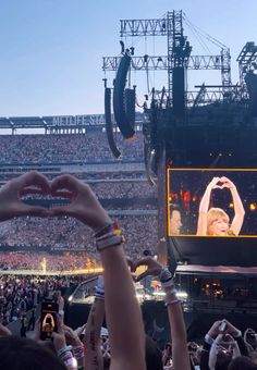 people are holding their hands up in front of a large screen at an outdoor concert