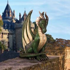 a statue of a dragon sitting on top of a stone wall next to a castle