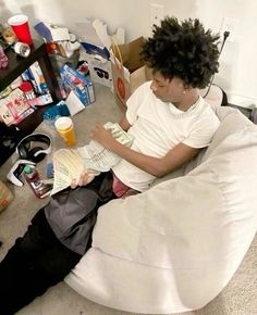 a man sitting on a bean bag chair reading a newspaper and drinking beer in his hand