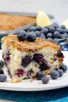 a piece of blueberry coffee cake on a white plate with fresh blueberries around it