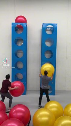 two men are playing with large balls in an office setting that is painted blue and yellow