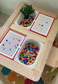 two trays filled with different colored beads on top of a wooden table next to a potted plant