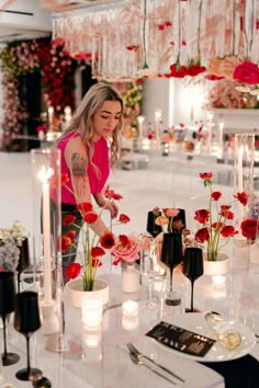 a woman standing over a table filled with flowers and candles