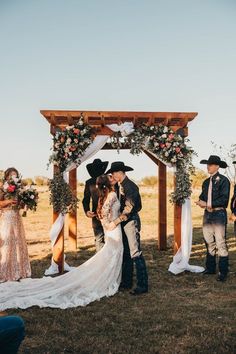 a bride and groom kissing in front of an outdoor wedding arch with flowers on it