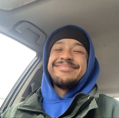 a man wearing a blue hoodie is smiling in the back seat of a car