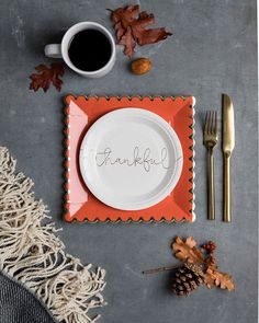 a place setting with an orange and white plate, silverware, napkins, and autumn leaves