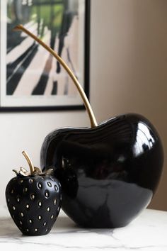 an apple and a strawberry shaped sculpture on a marble countertop in front of a painting