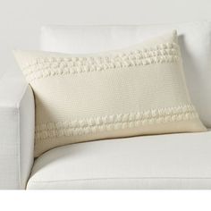 a white couch with a decorative pillow on it's back and the cushion is made out of knitted fabric