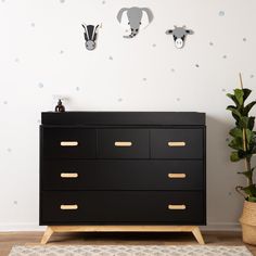 a black dresser with gold handles next to a potted plant and two wall mounted animal heads