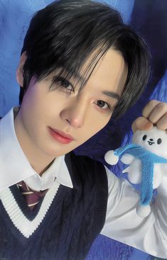 a young man holding a stuffed animal in his right hand and posing for the camera