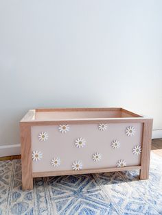 a wooden box sitting on top of a blue rug next to a white wall with flowers painted on it