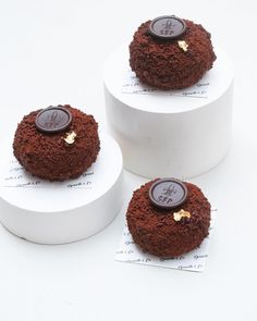 three round cakes with chocolate frosting and gold decorations on top are sitting in white boxes